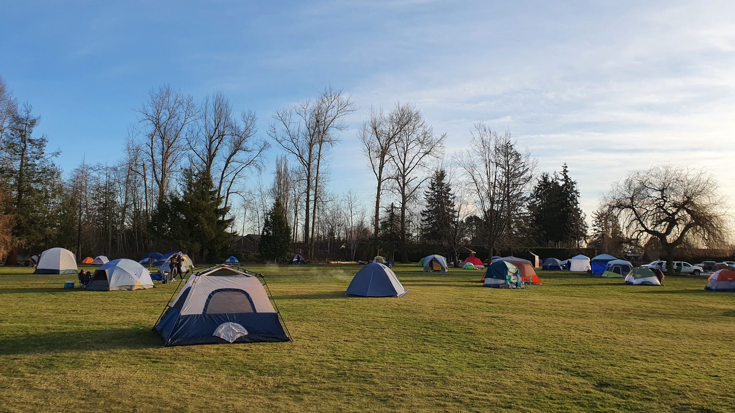 Several tents sit on a large grassy area with trees in the distance