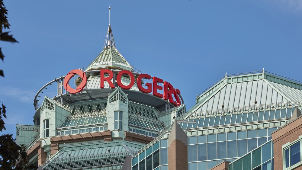 The exterior view of the Rogers Communications head office with its large red sign on top of a glass building