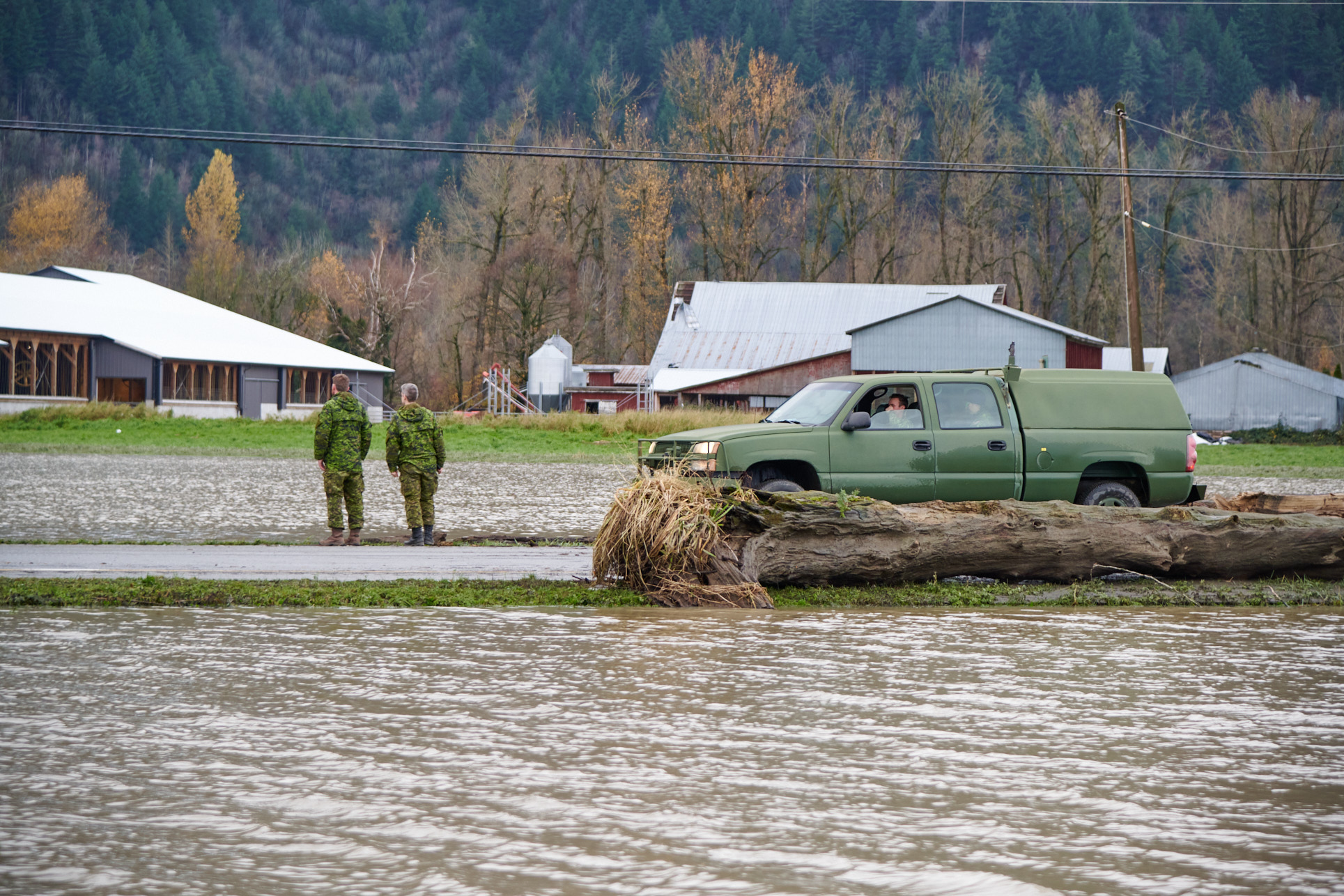 Two Canadian Armed Forces members stand at the edge of a flooded field