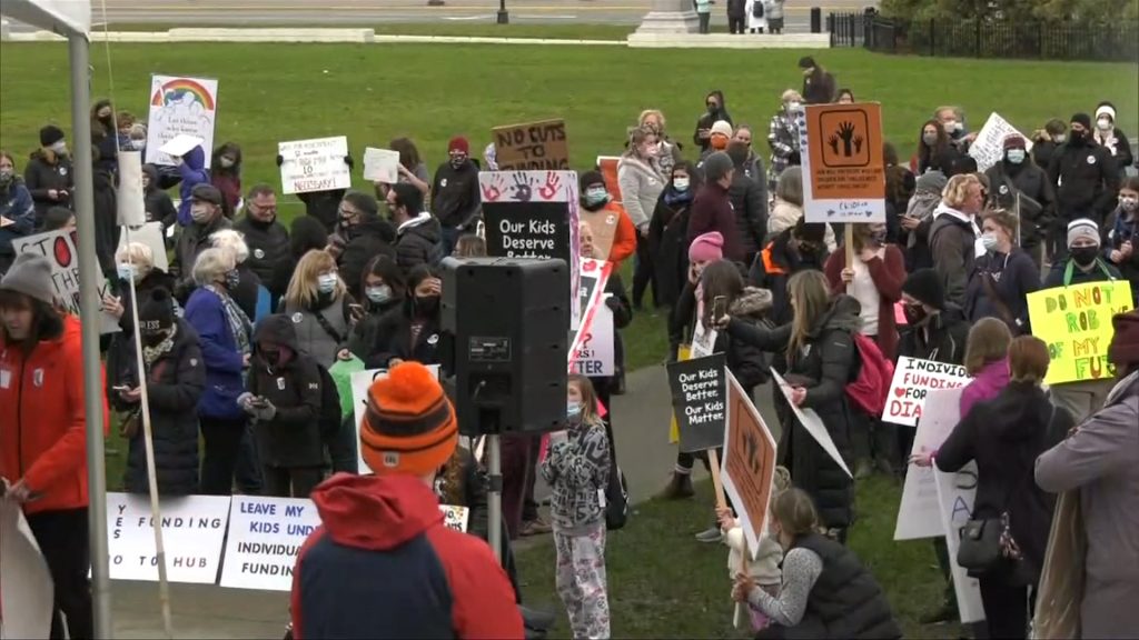 Parents gather in front of the B.C. Legislature carrying signs and making speeches against autism funding changes