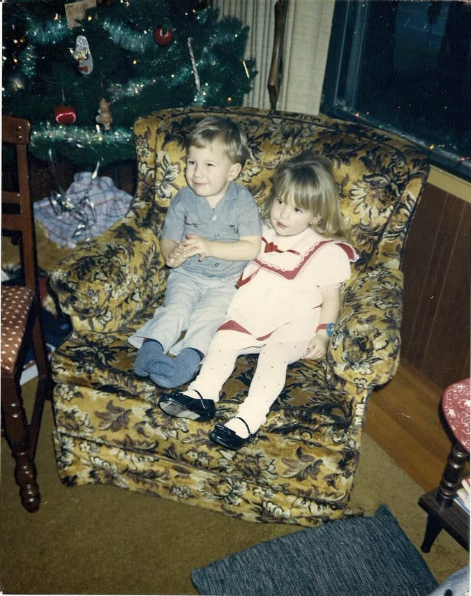 Two young children sit on an armchair side by side