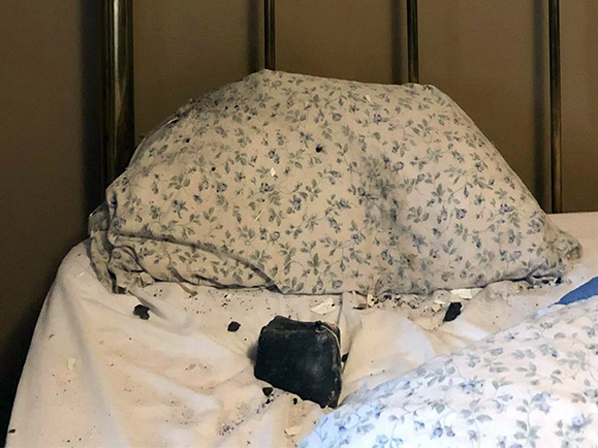 A large meteorite sits on a bed after crashing through a roof, debris scattered around it