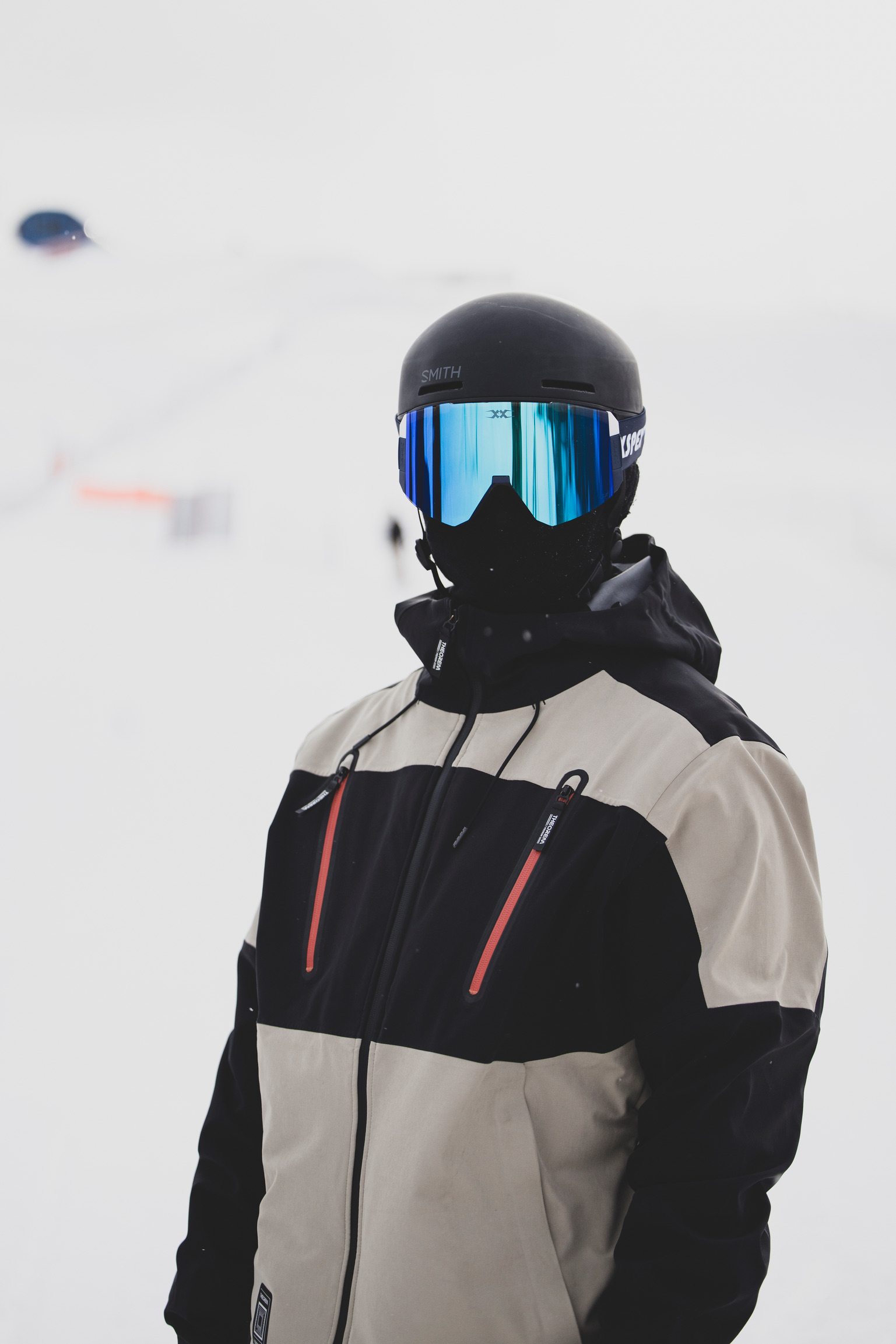 A snowboarder wearing a black helmet, reflective blue goggles, and a black and white jacket