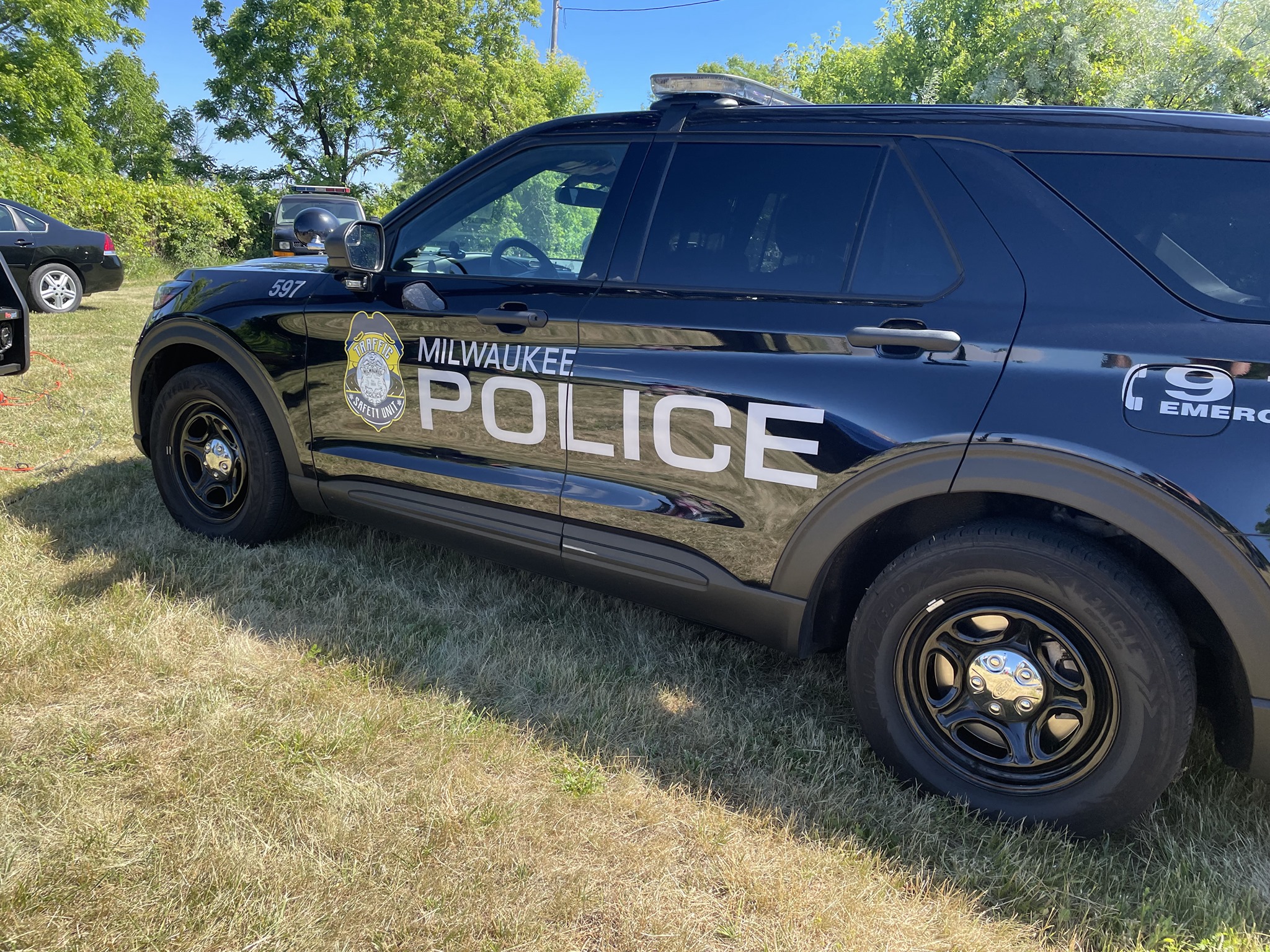 A dark SUV parked on some dry grass. The vehicle has the words 'Milwaukee Police' written on the side, with police written in larger letters