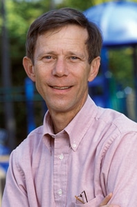 A man wearing a light coloured shirt smiles while sitting for a portrait photo