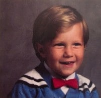 A photo of Michael Dunahee wearing a blue shirt with white and black shoulder pads. He's wearing a red bowtie and is smiling