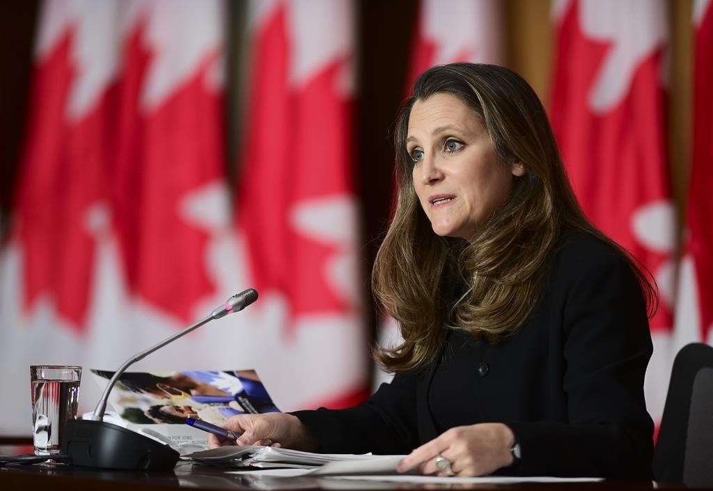 Chrystia Freeland stands at a podium, with a wall of Canadian flags pictured behind her