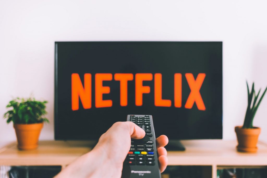 A person points a remote control at a TV with the NETFLIX logo in big on the screen