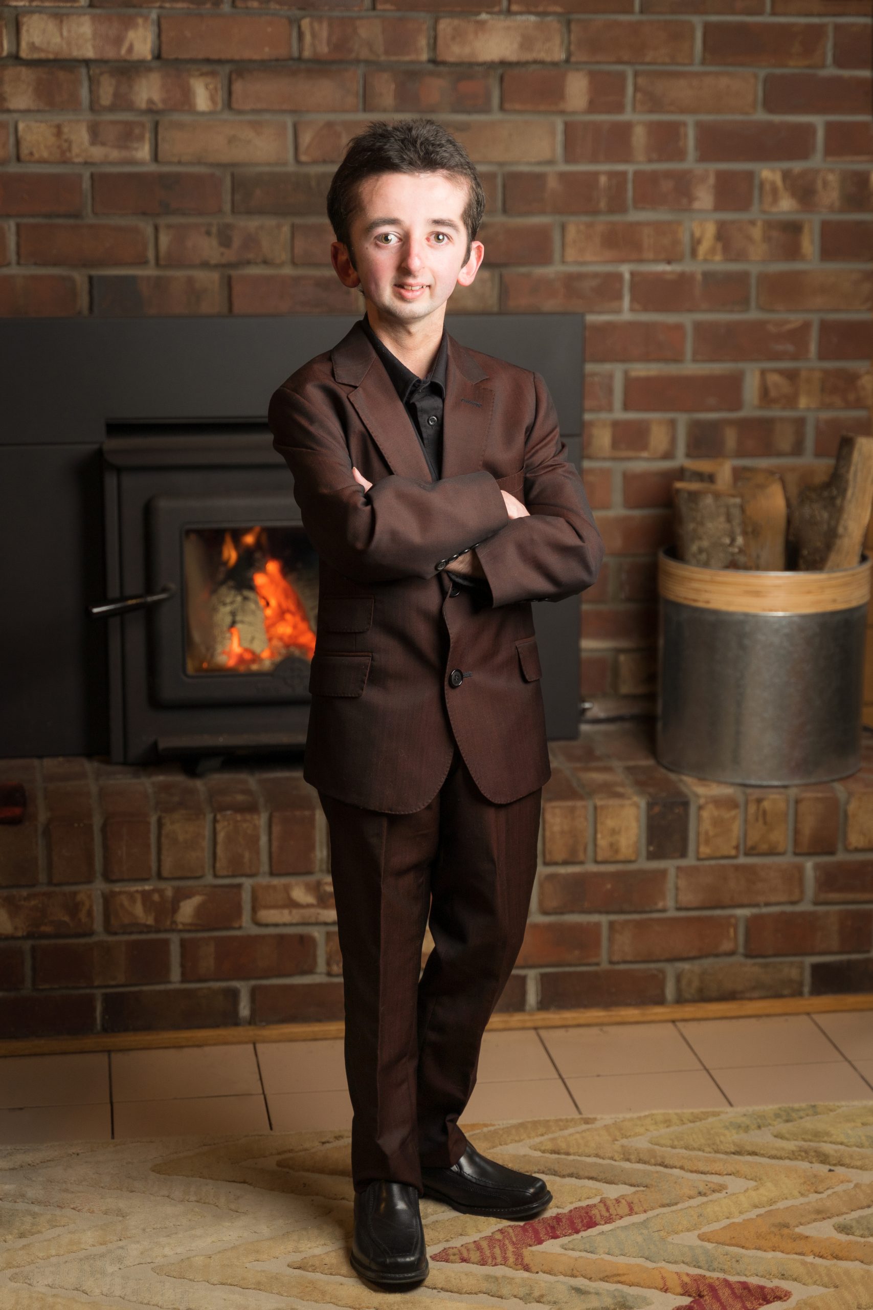 Casey Wright, the 2022 Courage To Come Back Award recipient in the Youth category, stands wearing a dark coloured suit in front of a fireplace, his arms crossed in front of him