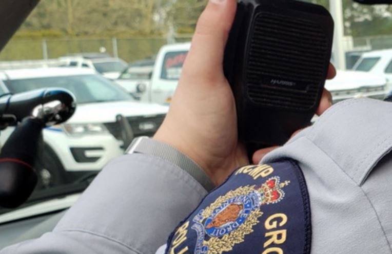 An RCMP officer's shoulder patch is seen as a hand holds up a radio in a vehicle