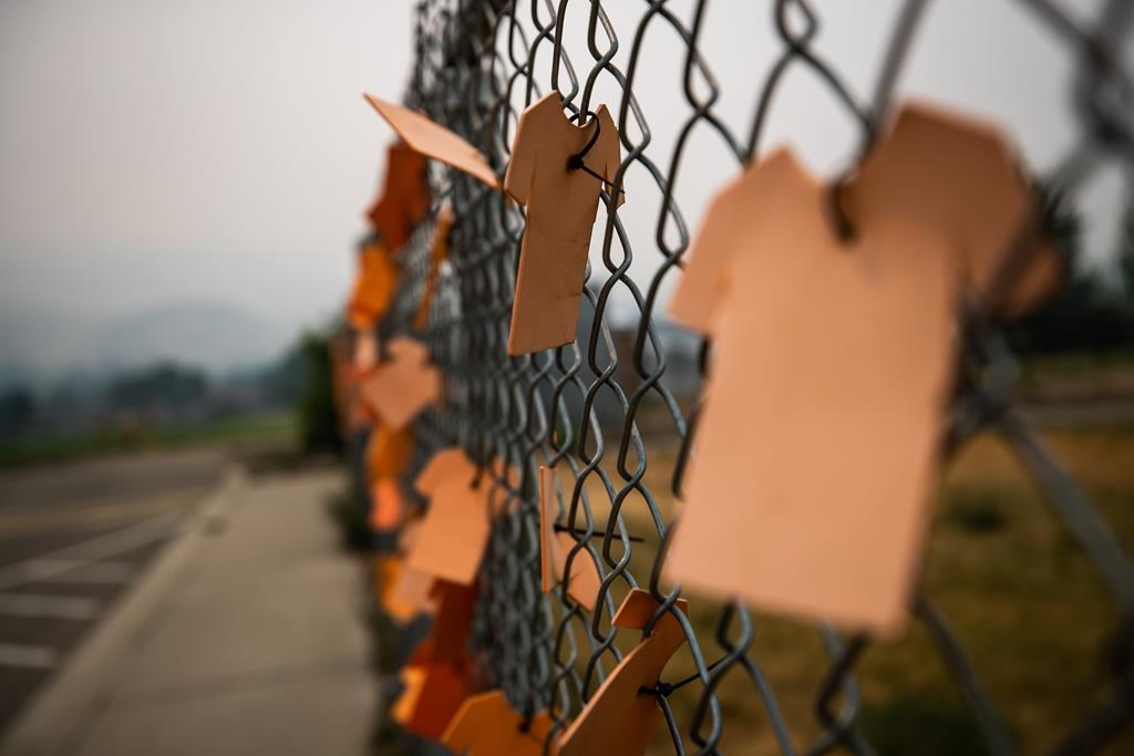 Cutouts of orange t-shirts are hung on a fence