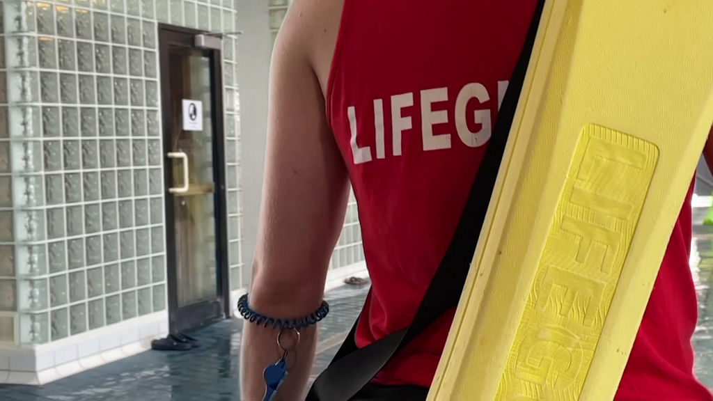 The back of a lifeguard's shirt with half of the word 'lifeguard' visible under a floatation device