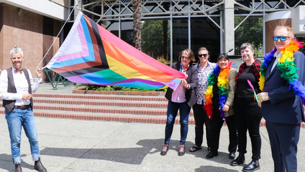 Victoria Mayor Lisa Helps stands on the left holding a Pride flag along with several others outside city hall