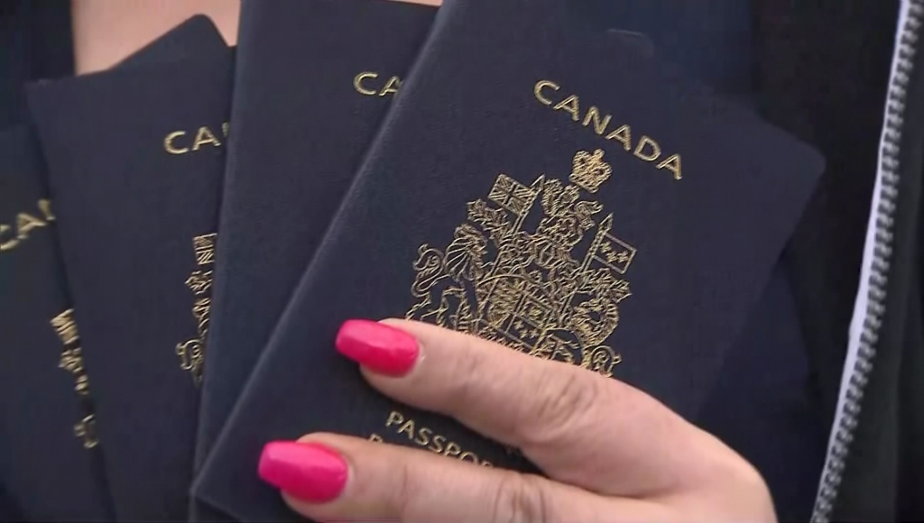 Four Canadian passports are held up in a person's hand