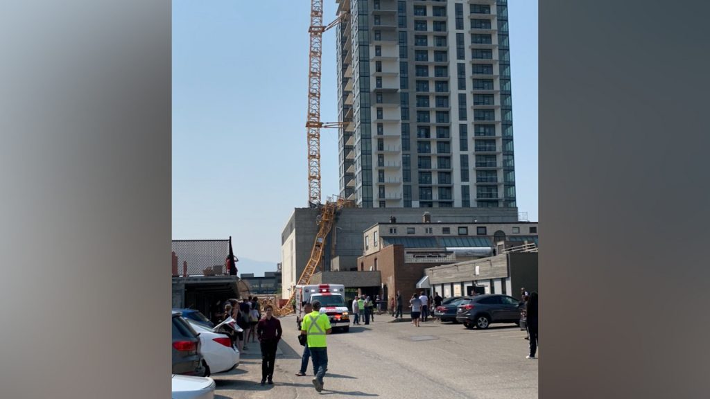 A crane is seen collapsed against a building in Kelowna as people look on from a distance