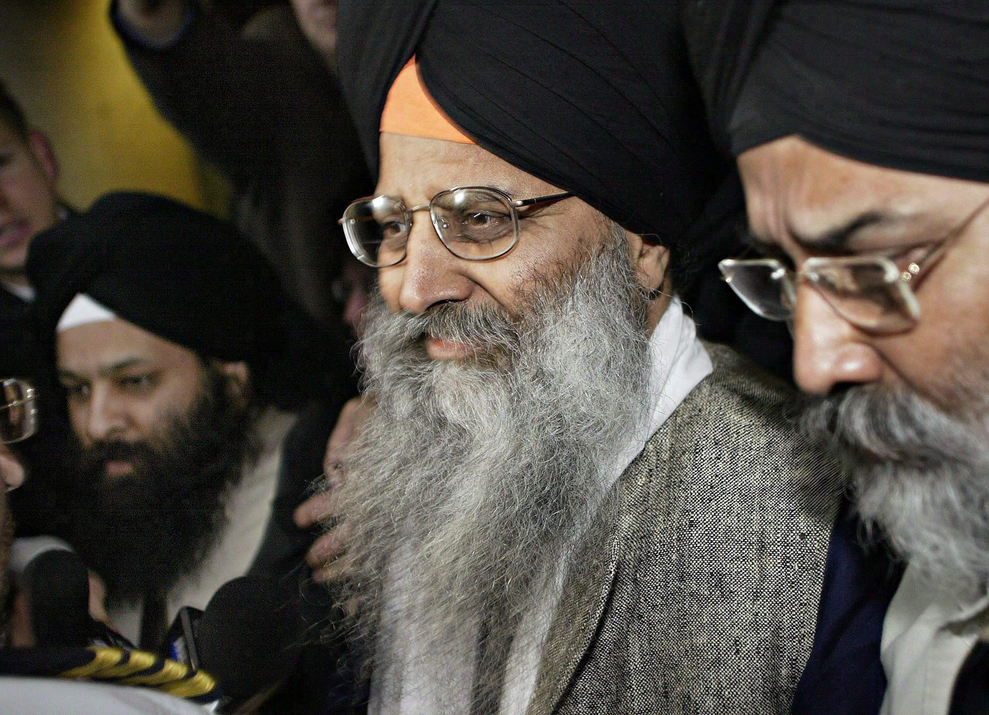 Three men wearing turbans stand in a row, each of them with long beards