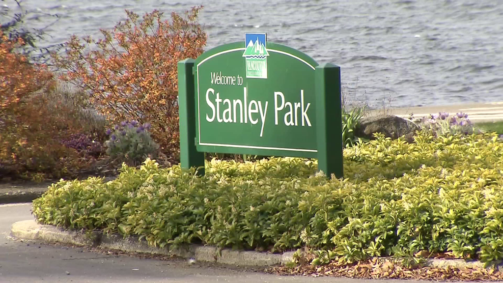 A sign for Stanley Park in Vancouver is pictured standing in a bush, the ocean slightly visible in the background behind it