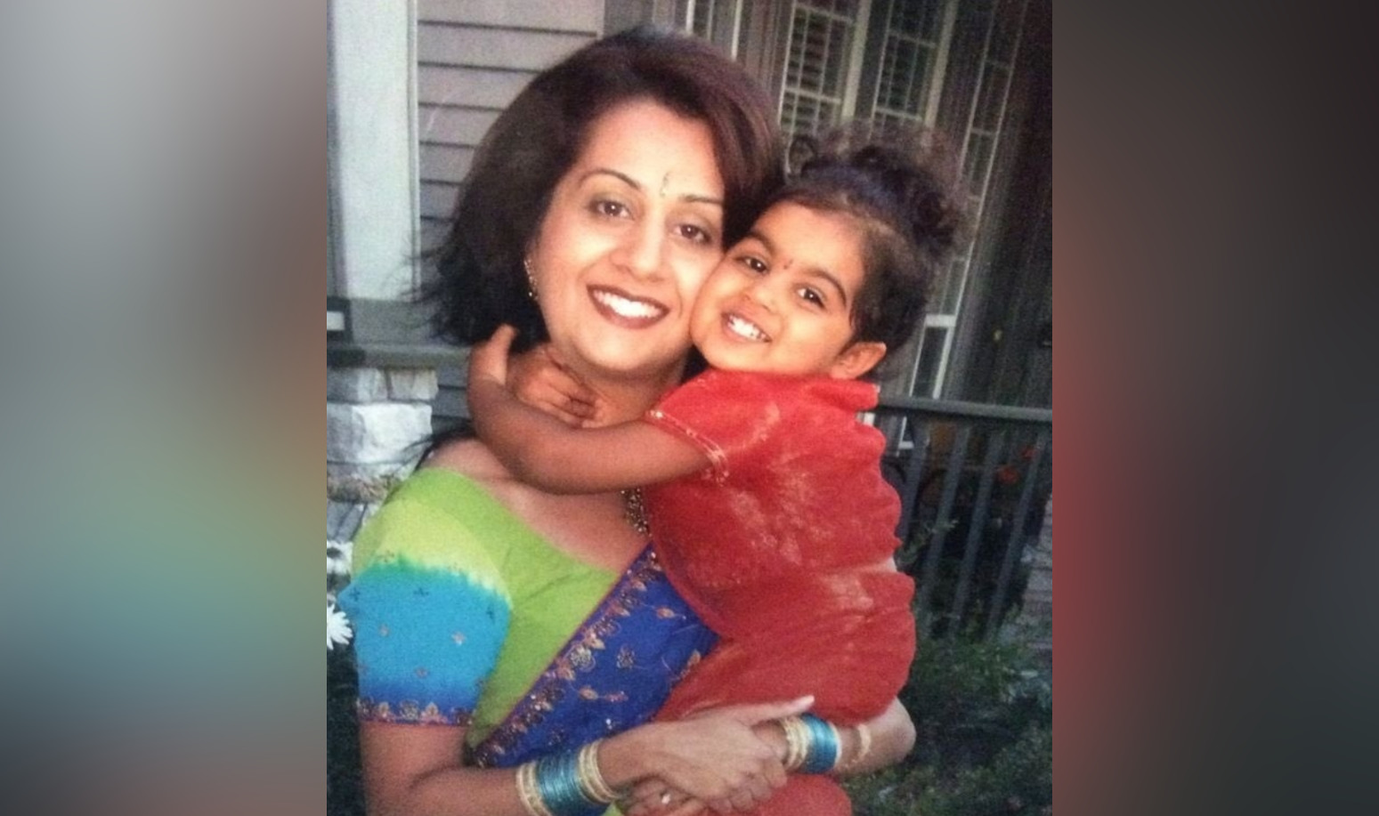 A woman wearing brightly coloured clothes holds a young child who has their arms wrapped around her neck in an embrace