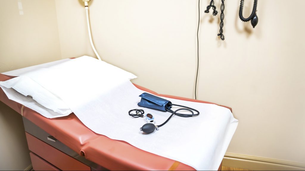 A doctor's examination room has various instruments laying on an exam table