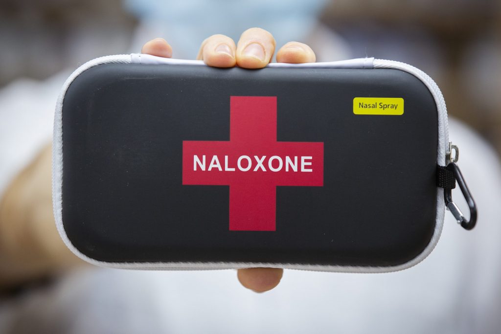 A Naloxone kit is held up by a hand in front of a blurred background