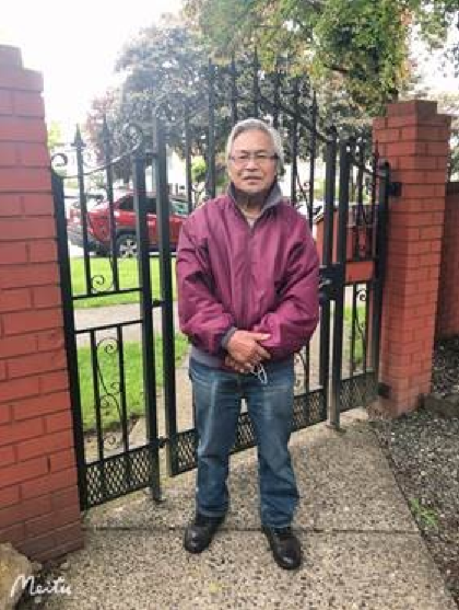 An image of a man standing outside by a fence and brick column