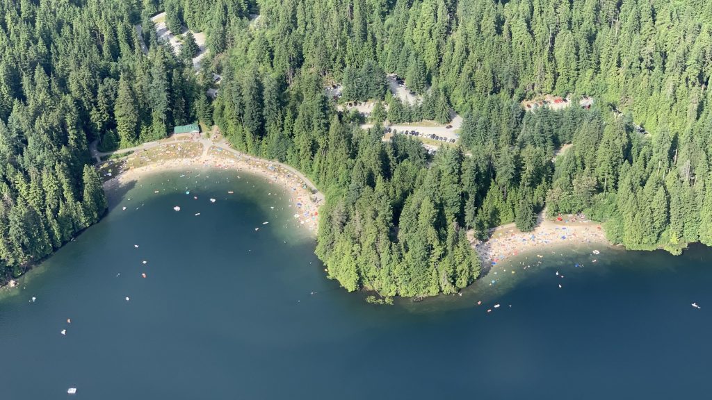 View looking down on waterfront with green trees and sandy beach