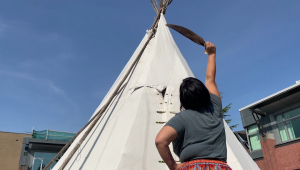 woman with feather in front of tipi