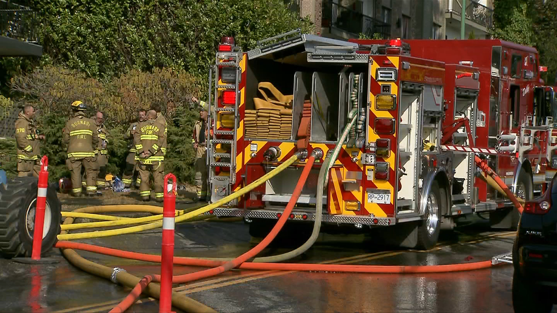 A Burnaby fire truck at the scene of a fire in Capitol Hill, with hoses laid out of the back of the vehicle and crews in the background