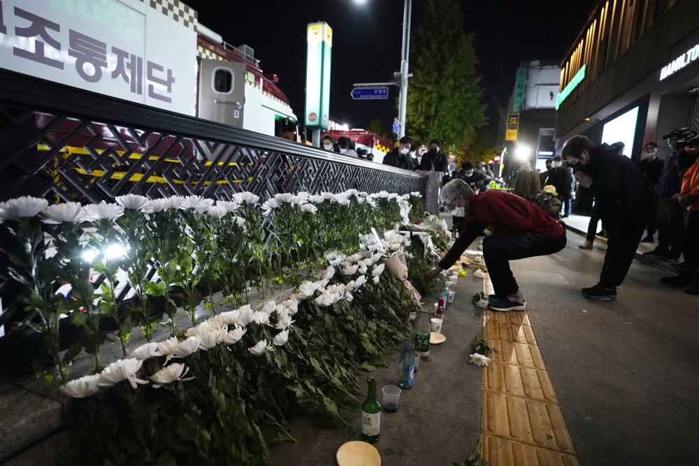A woman places flowers to pay tribute for victims near the scene of a deadly accident in Seoul, South Korea, Sunday, Oct. 30, 2022, following Saturday night's Halloween festivities. A mass of mostly young people among tens of thousands who gathered to celebrate Halloween in Seoul became trapped and crushed as the crowd surged into a narrow alley, killing dozens of people and injuring dozens of others in South Korea’s worst disaster in years