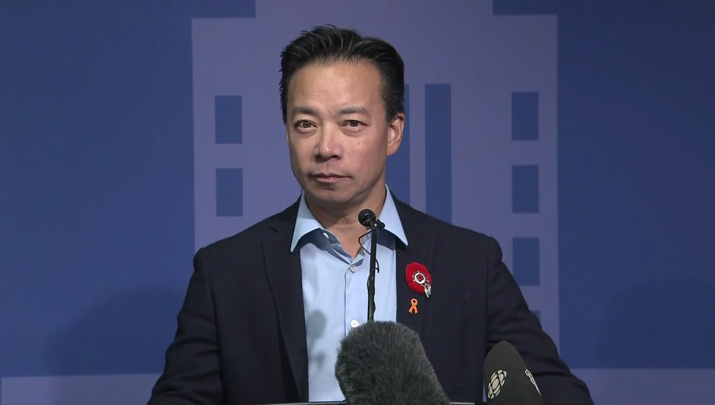 Vancouver Mayor Ken Sim stands at a podium with a blue background