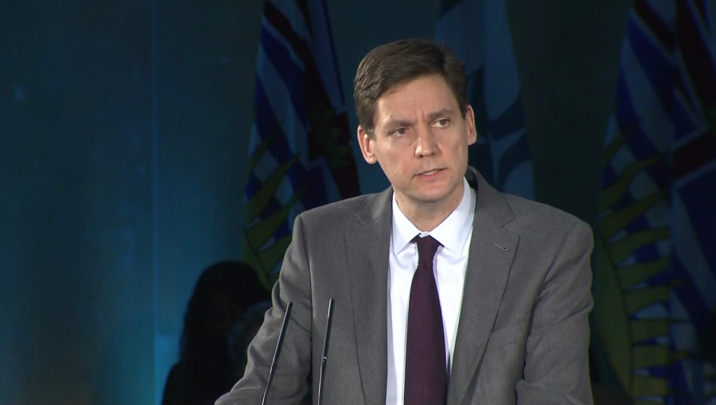 David Eby speaks at a podium with B.C. flags in the background