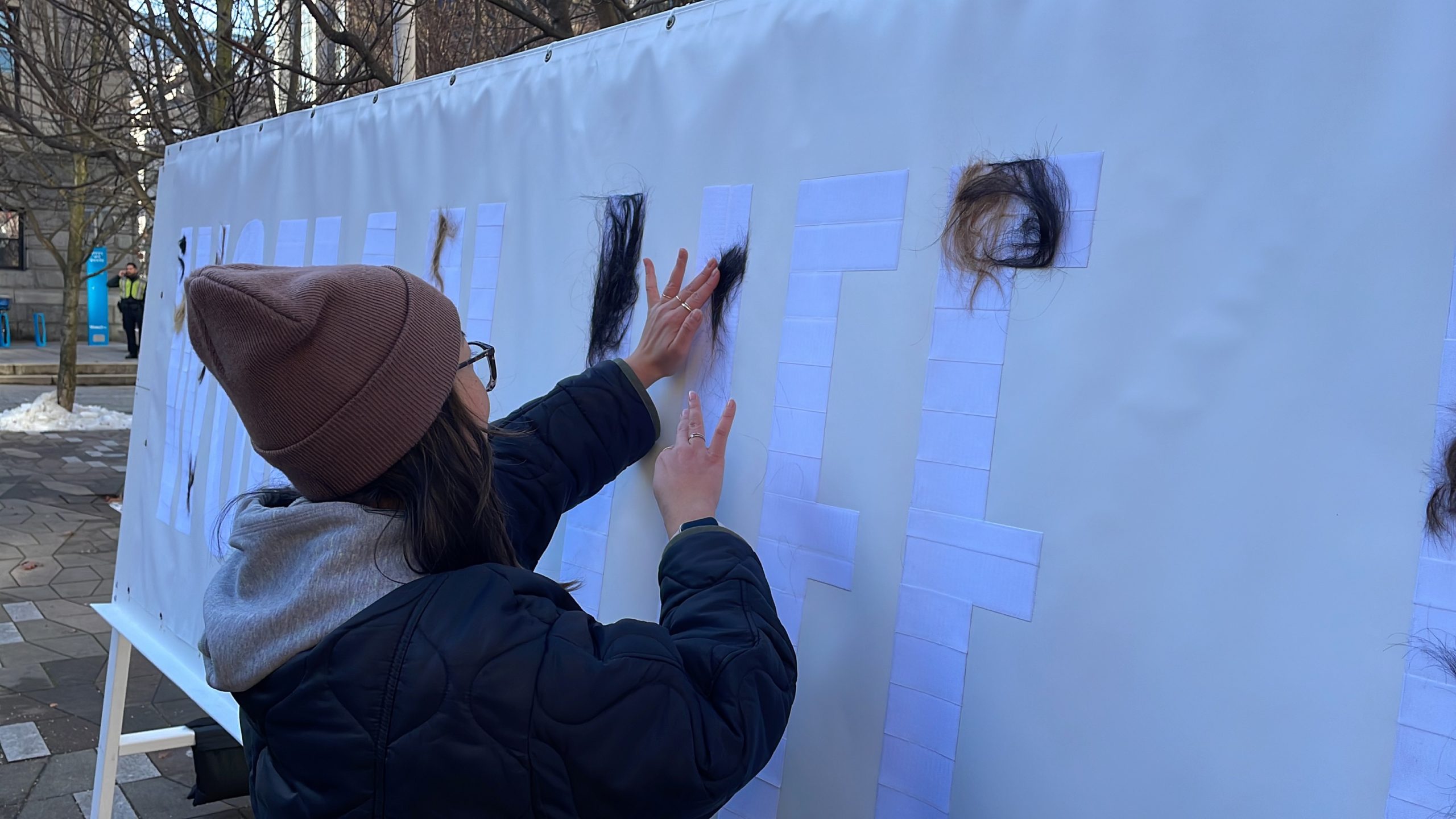 A woman glues hair to a wall that's part of a demonstration in solidarity with the women of Iran