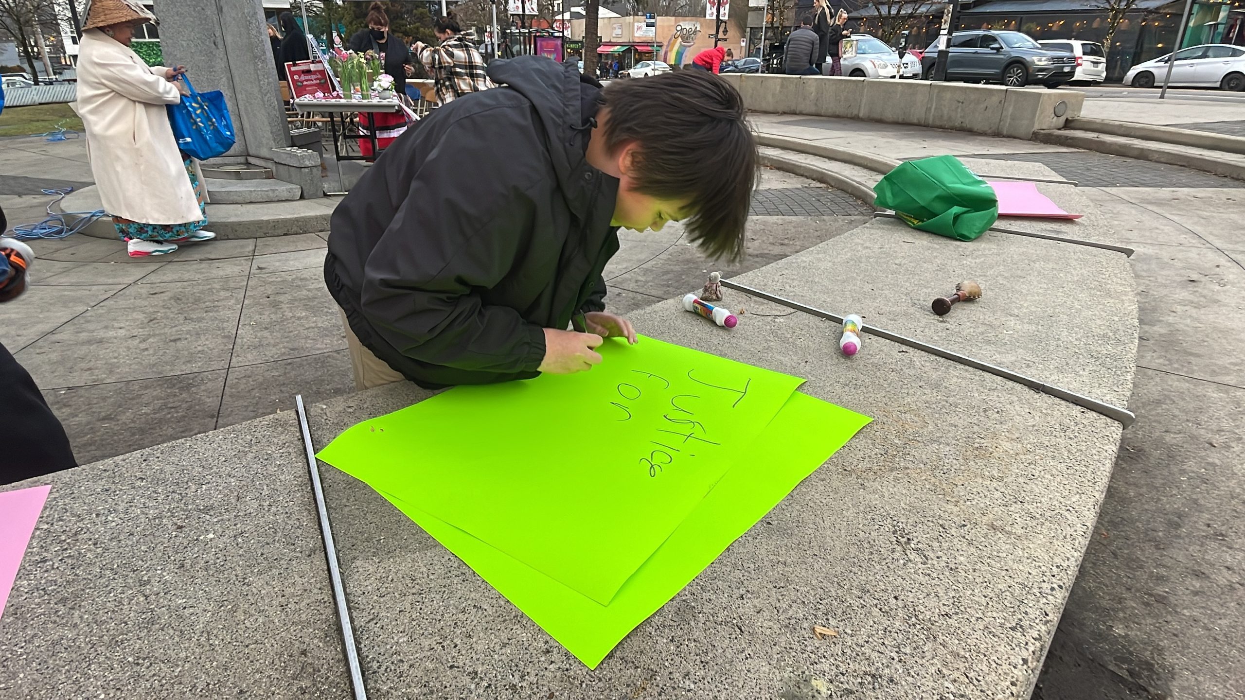 A person drawing on a neon green sign at a vigil in honour of murdered and missing Indigenous women