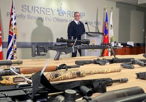 man stands at podium with guns on table in front