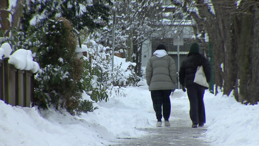 People walk down a snow covered sidewalk