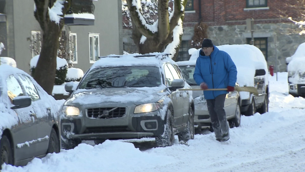 Person carries broom while clearing car of snow