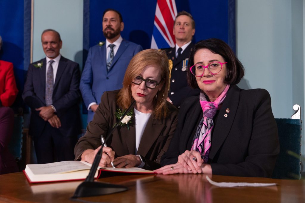 tow women sit at a table and sign papers