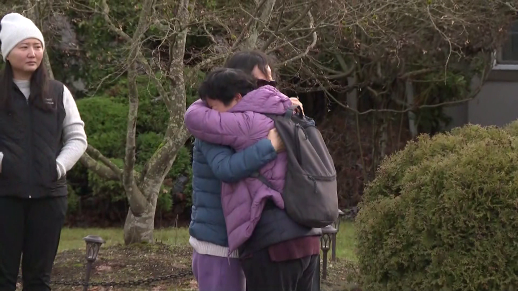 Two people hugging outside a Surrey home where three people were found dead