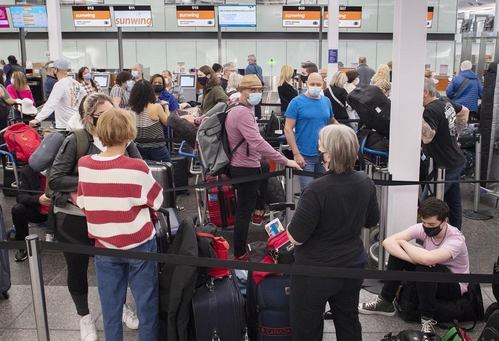 Travellers waiting in line at an airport, with orange Sunwing signs and information display screens in the background.