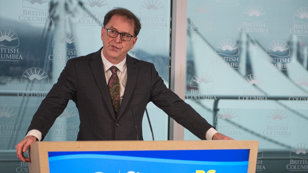 Adrian Dix stands at a podium with the Canada Place sails in the background