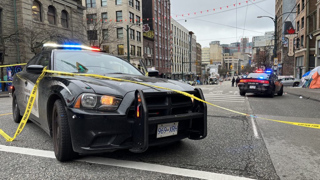 A police cruiser sits on East Hastings Street covered in police crime scene tape