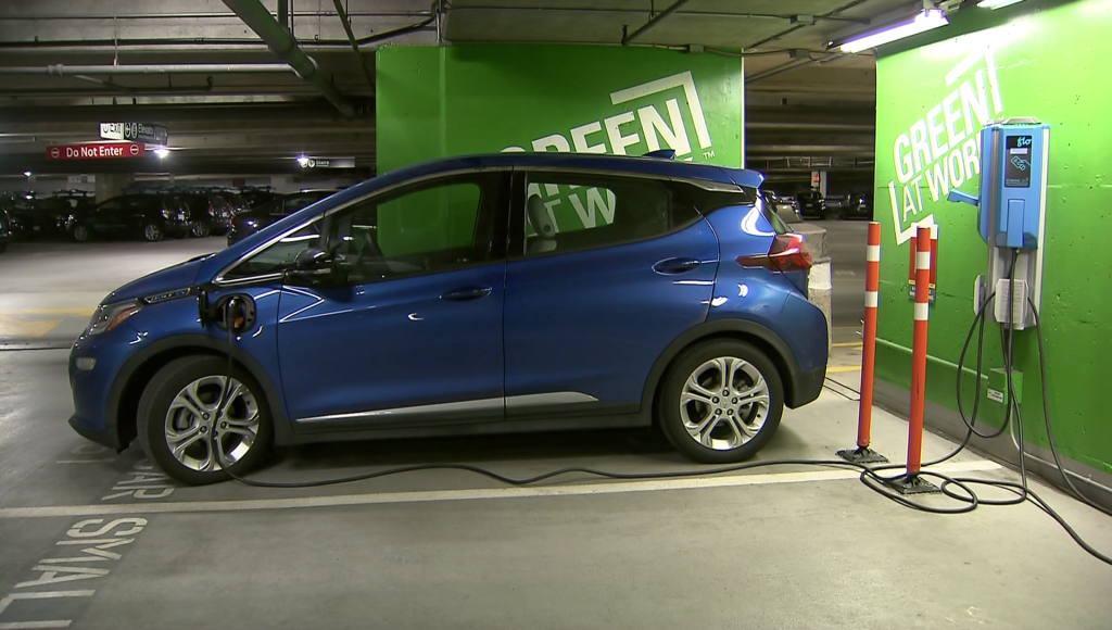 An electric vehicle is shown plugged into a wall in a parking garage.