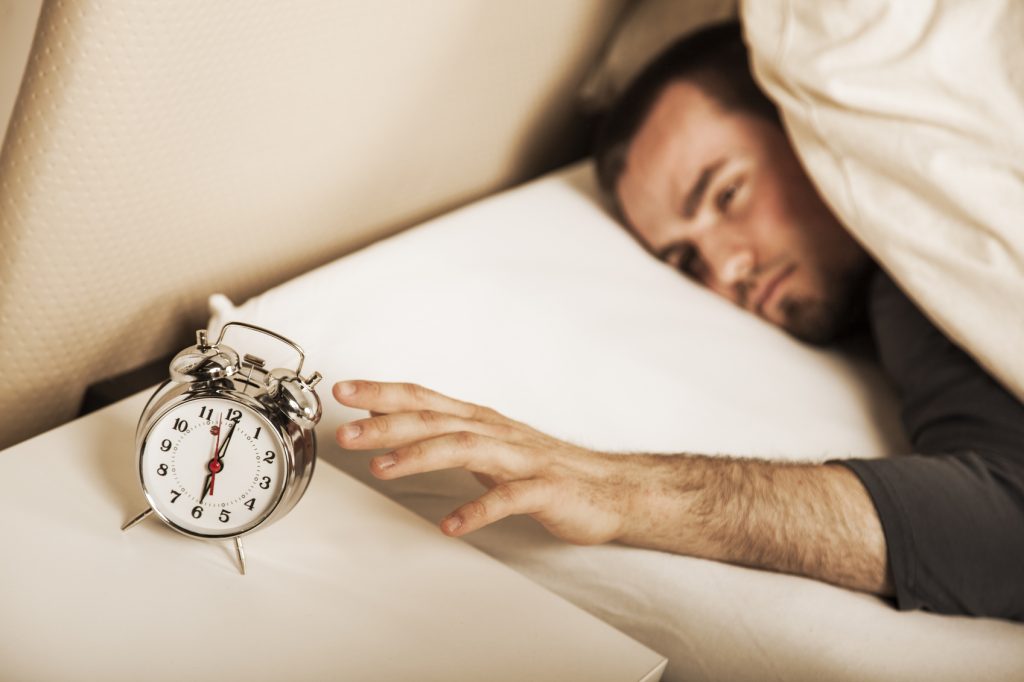 A stock image of a man reaching for an alarm clock.