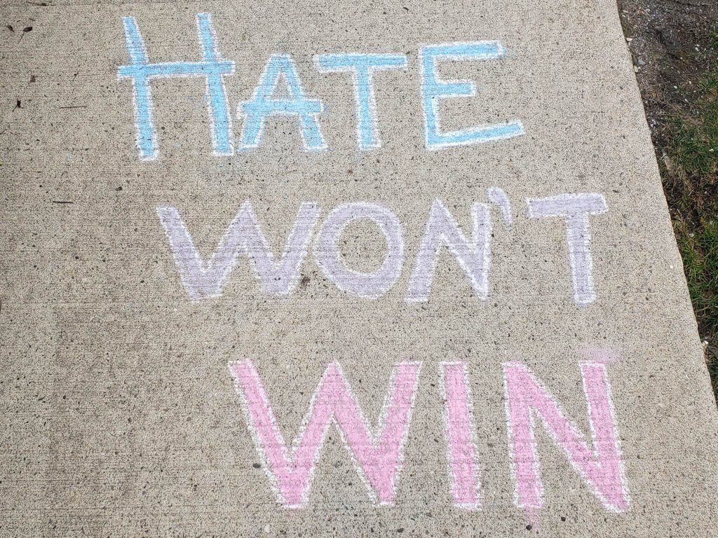 A colourful message in yellow, blue and purple that says hate won't win is placed on a sidewalk after a house was spray-painted