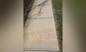 a sidewalk in Langley has been tagged in orange paint with the words up ahead nazi 