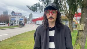 A film worker in bc wears large red round glasses, a hat and a striped tshirt. he says workers in the BC's film industry are having a hard time finding work. 