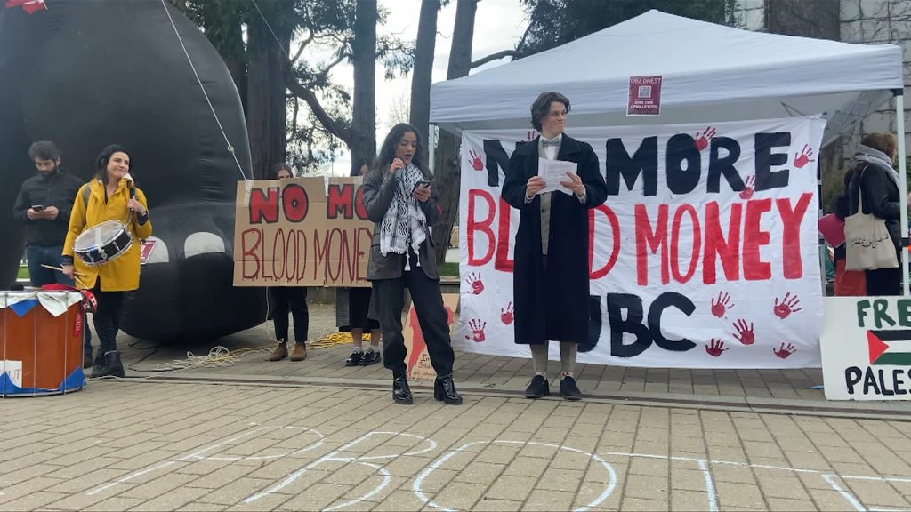 students gathered at the university of british columbia to call for the school to make better investments. two people stand in front of a sign that reads no more blood money ubc.