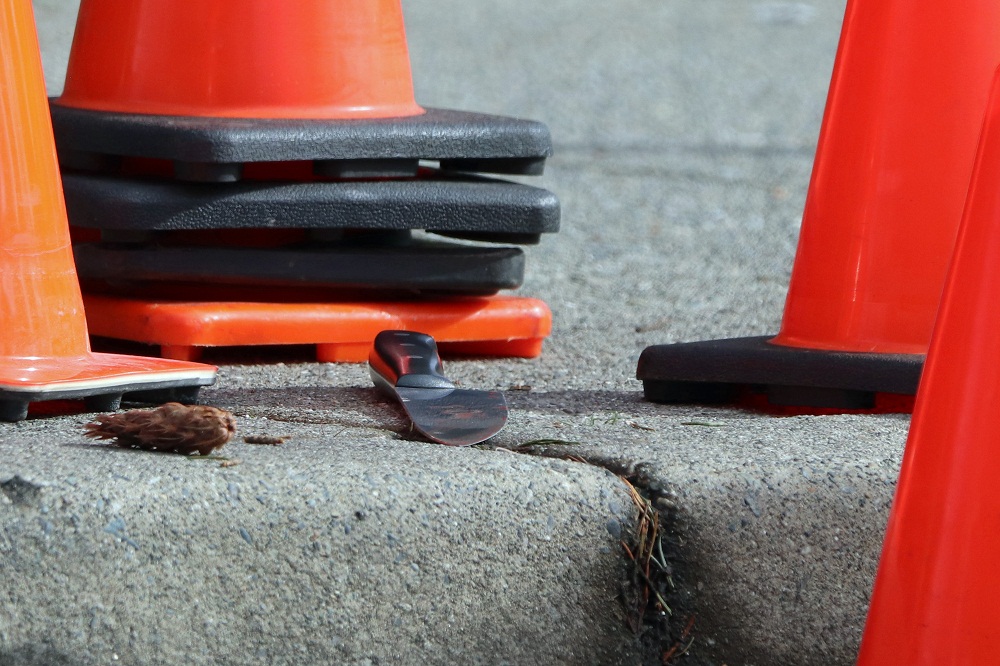 A knife is shown sitting on the sidewalk in front of traffic cones.