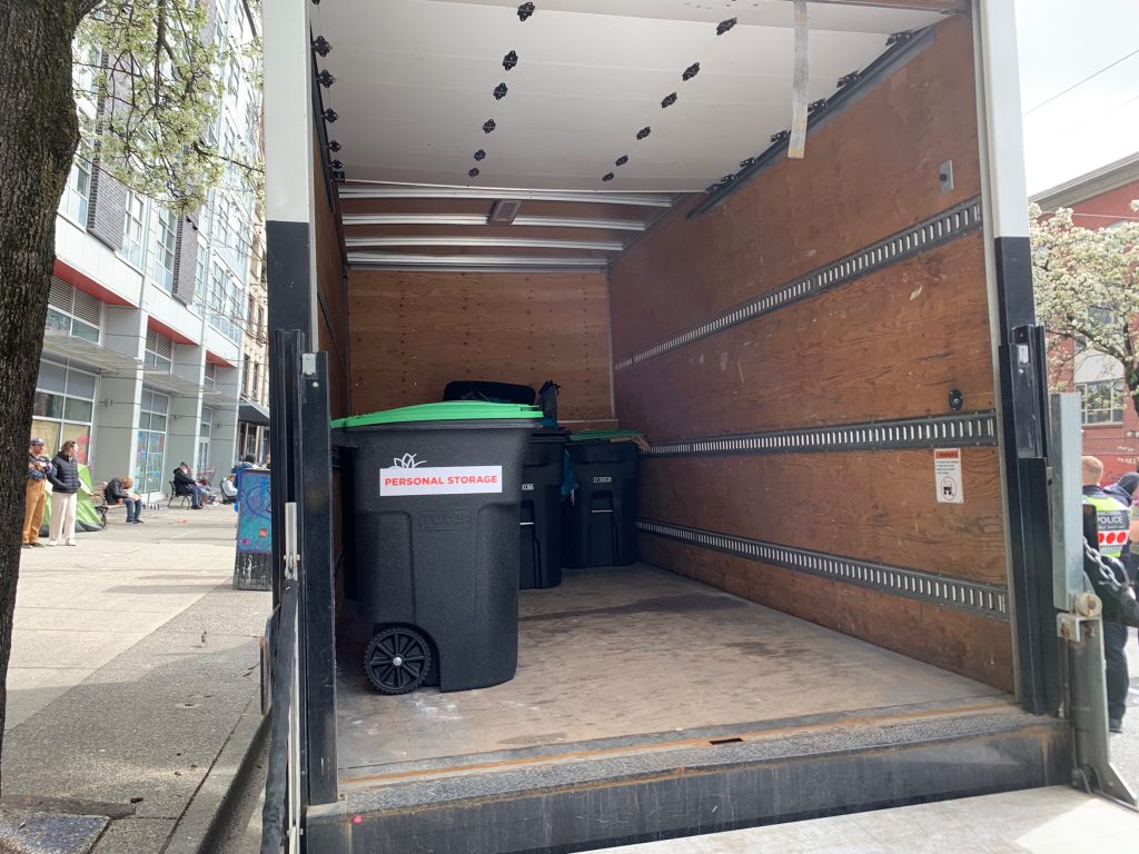 a black garbage bin with the word personal belongings is shown in the back of a truck. On Wednesady part of East Hastings street was shut down as part of the city's plan to decamp the area.