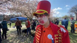 a person stands in what looks like a red uniform and hat with white face paint and red around the eyes and mouth. This comes as BC marked 7 years of a public health emergency of the toxic drug crisis